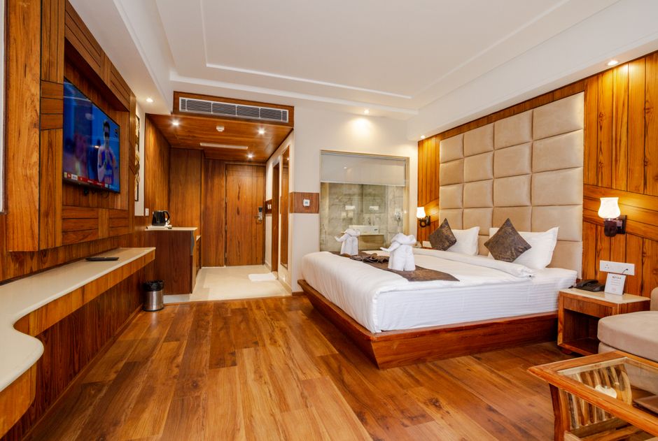 A king room panelled in warm wood, with a wall-mounted smart TV facing a generous bed dressed in white linen.