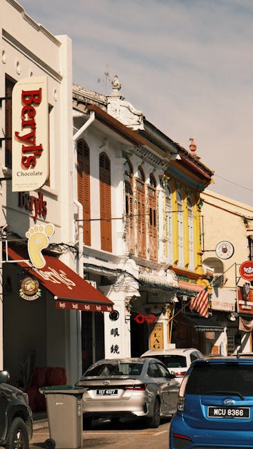 A row of old Alor Setar shophouses with timber louvre shutters, awnings and shopfront signs lining the street.